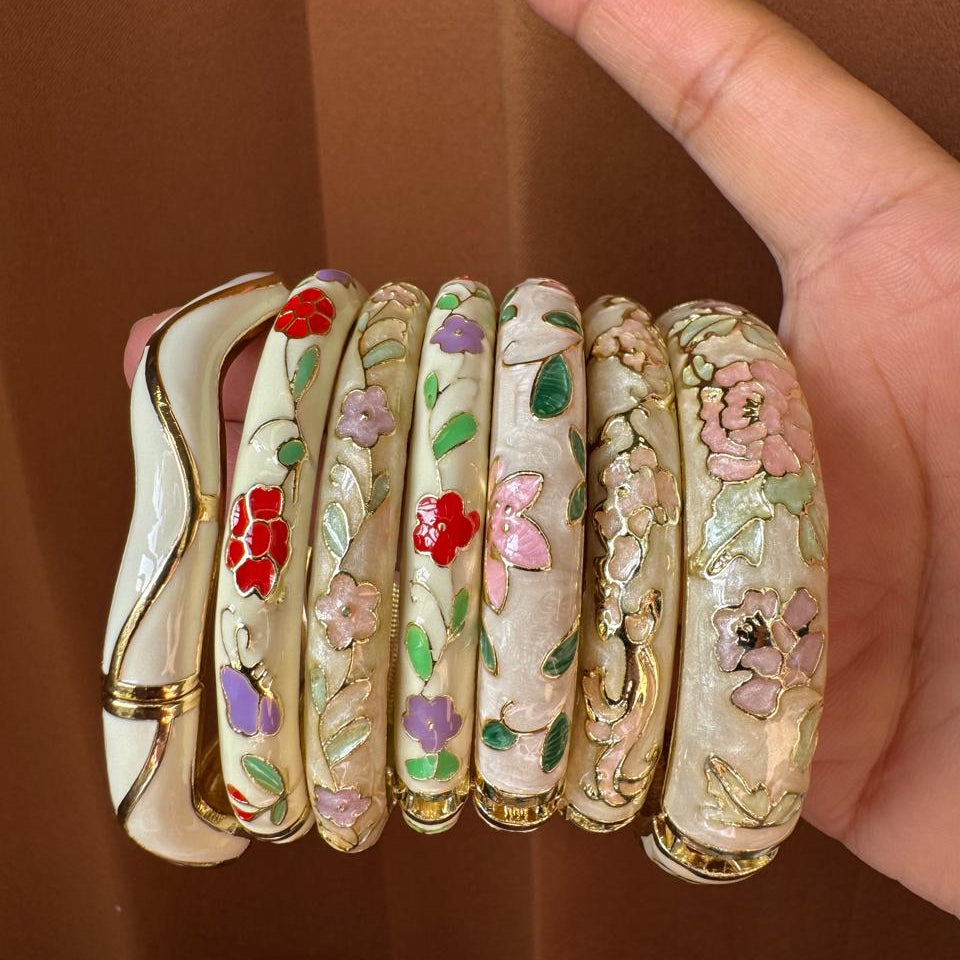 Set of decorative bangles with floral patterns held by a hand against a brown background