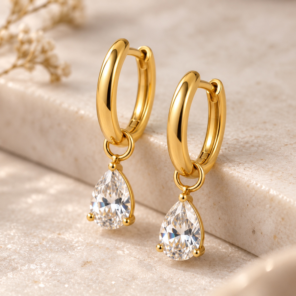 Close-up of Sereia gold-tone huggie earrings showing faceted pear-shaped clear crystal drops